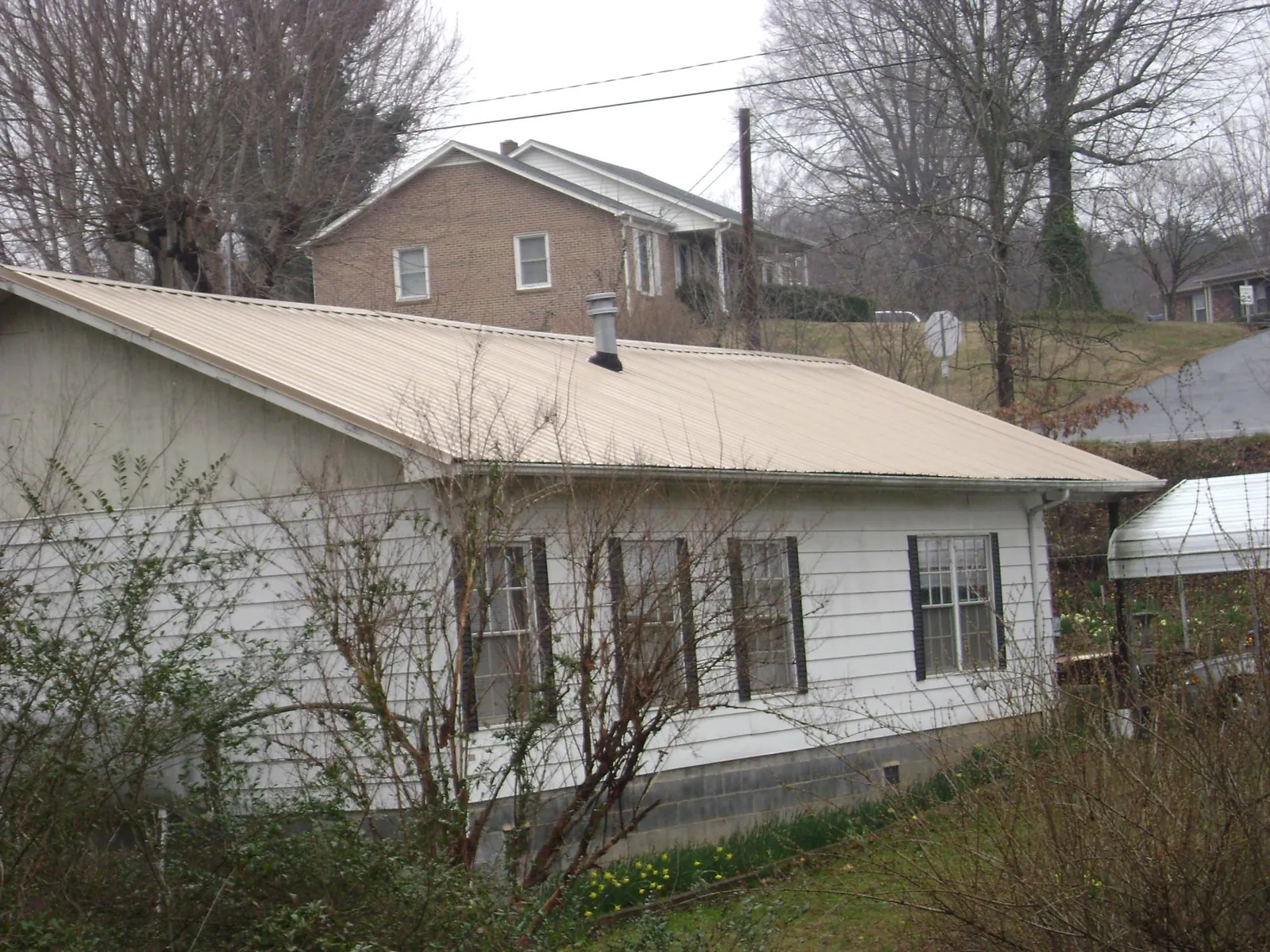 Tan metal roof on a white sided house set into a hillside — Commercial Roofing by Roofing Brothers in Ada